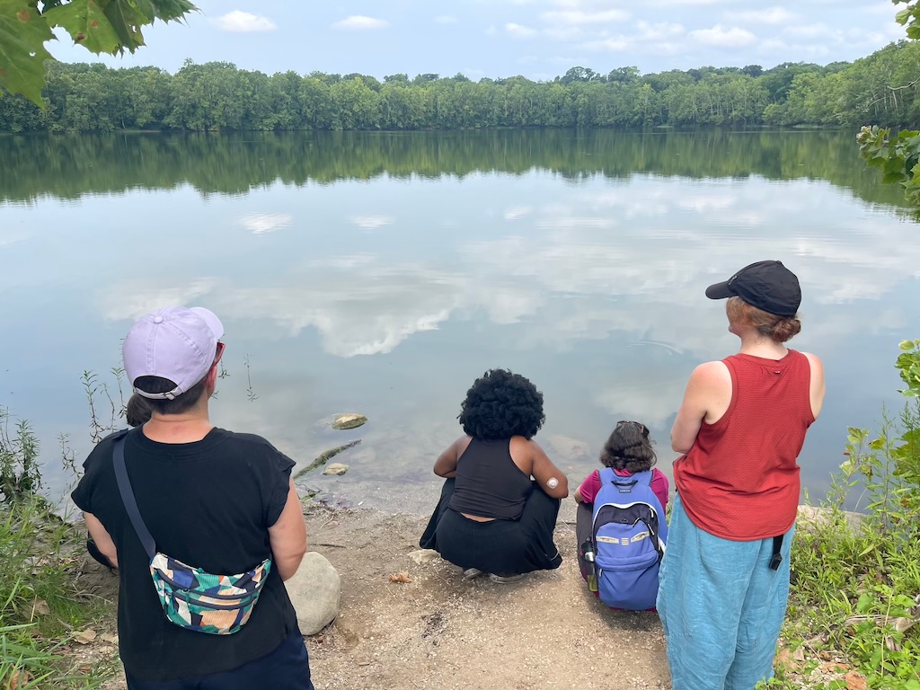 Four humans gathered looking at the lagoon at the 100 Acres in Indianapolis.